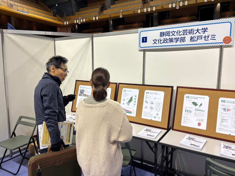 大学サミットにて来場者に説明する学生の写真