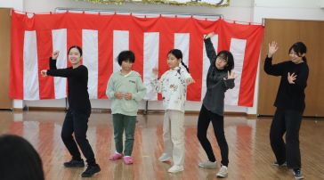 小学生の前で挨拶をする学生の画像